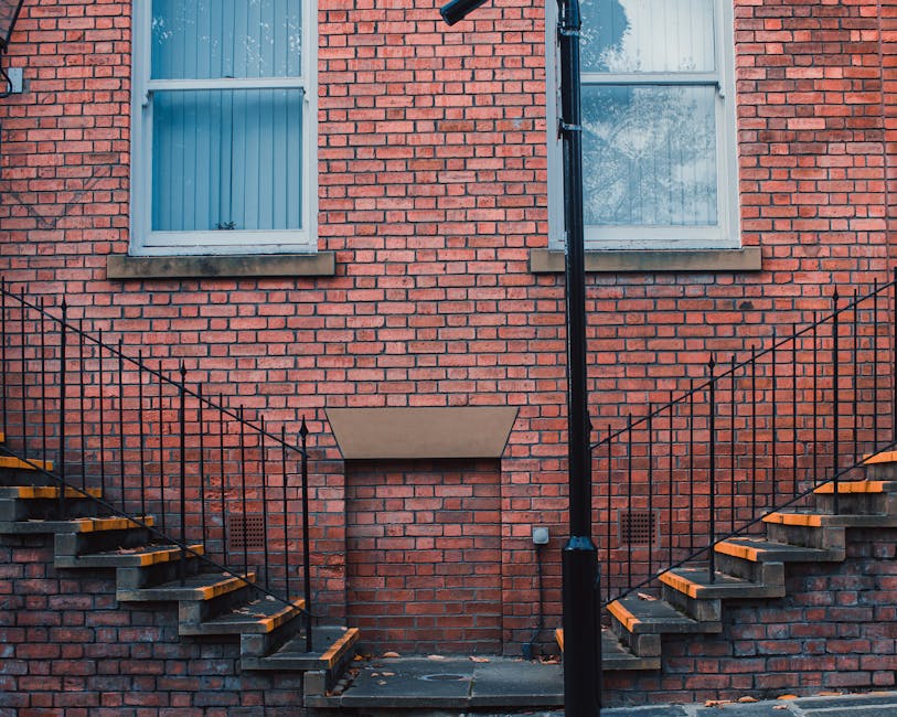 Inside a property showing a narrow staircase with black-painted wooden steps and a wooden handrail mounted on the wall, which is tiled with white rectangular subway tiles. The staircase appears steep